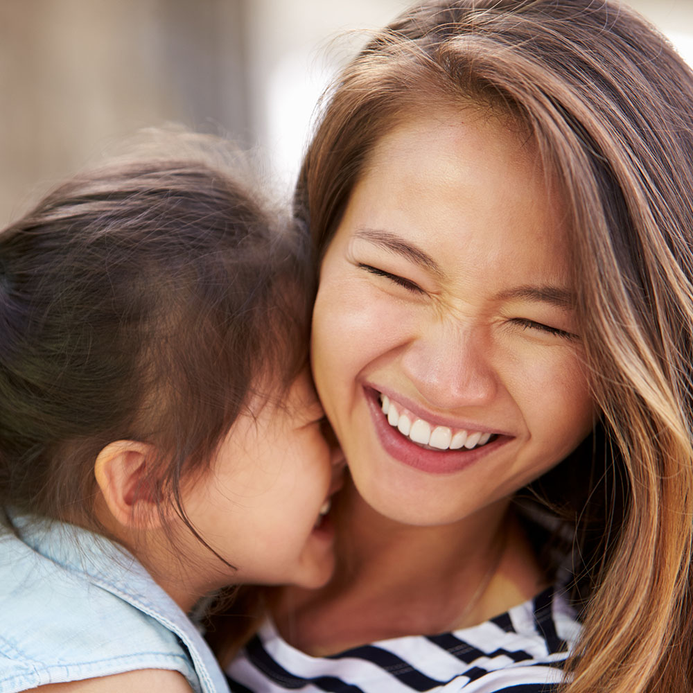 A woman with a young child, both smiling, sharing an affectionate moment with their faces close together.